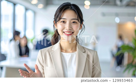 一位身穿米色西裝的日本女性在開放式辦公室裡與同事微笑交談的肖像 129933463