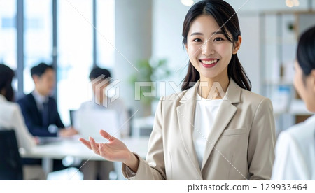 一位身穿米色西裝的日本女性在開放式辦公室裡與同事微笑交談的肖像 129933464