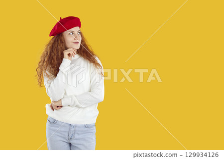 Thoughtful curly girl in red beret and white sweater looking on copyspace on yellow background. Thoughtful curly girl in red beret and white sweater looking on copyspace on yellow background. 129934126