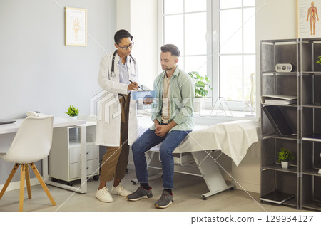 Male patient sitting on examination table, female doctor holding clipboard, explaining test results Male patient sitting on examination table, female doctor holding clipboard, explaining test results 129934127
