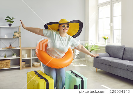 Fat woman in hat and sunglasses getting ready for holiday trip standing with suitcases at home 129934143