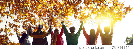 Group of happy friends standing with raised hands at sunset 129934145