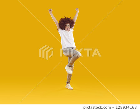 Preteen smiling boy happily jumping with his hands raised 129934168