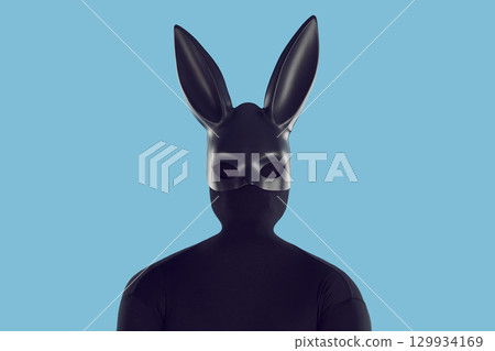 Portrait of man in black bodysuit and long eared bunny mask isolated on blue background Portrait of man in black bodysuit and long eared bunny mask isolated on blue background 129934169
