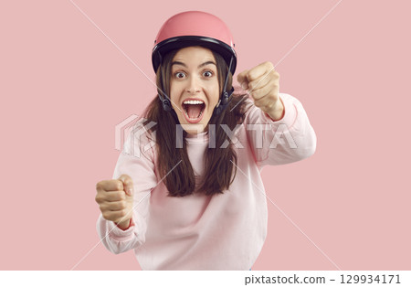 Funny woman in pink helmet with excited or scared face expression driving invisible car Funny woman in pink helmet with excited or scared face expression driving invisible car 129934171