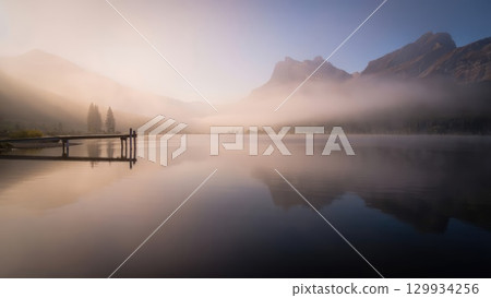 Misty mountain lake at dawn with calm water and pier, peaceful vertical landscape wallpaper for smartphones. Generative AI. 129934256