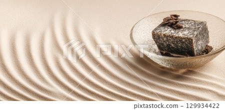 African Black Soap on Ripple-Textured Glass Tray with Neutral Cream Background 129934422