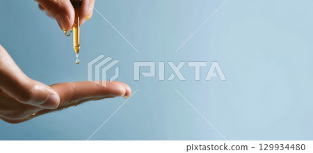 Minimalist Beard Oil Drop on Fingers with Soft Blue Background 129934480
