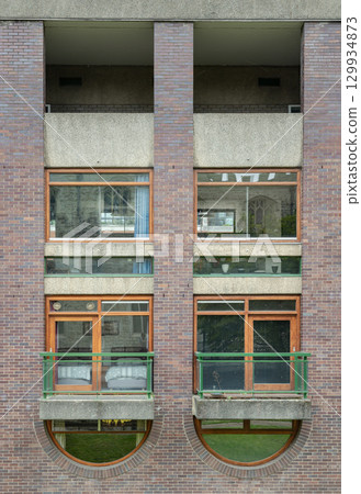 Residential units within the Barbican Estate, characterized by windows integrated with small balconies featuring green metal railings and prominent exposed brickwork. 129934873