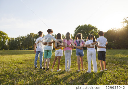 Group of teenage children look at sunset together during summer walk in green park. 129935042