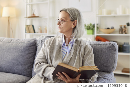 Calm mature woman spending leisure time at home alone, sitting on comfortable sofa Calm mature woman spending leisure time at home alone, sitting on comfortable sofa 129935048