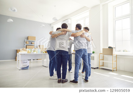 Group of volunteers standing together in circle and hugging during work in humanitarian center. Group of volunteers standing together in circle and hugging during work in humanitarian center. 129935059