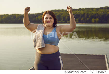 Fat woman in sportswear do winner's gesture clenching fists celebrating success in workout outdoors 129935074