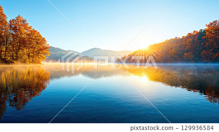 serene lake at dawn with mist rolling over still water, surrounded by vibrant autumn trees and rising sun 129936584