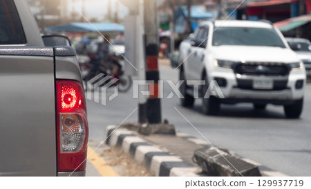 Rear side of pick up car with turn on brake light. Island of road with electric pole. with motorcycle in the middle of the road waits to make a U-turn. A car drives past from the opposite side. Rear side of pick up car with turn on brake light. Island of road with electric pole. with motorcycle in the middle of the road waits to make a U-turn. A car drives past from the opposite side. 129937719