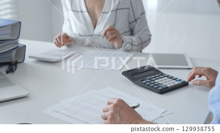 Professional team collaborating, reviewing financial reports, using calculator, analyzing data while working at sleek corporate workspace. Audit and taxes in business Professional team collaborating, reviewing financial reports, using calculator, analyzing data while working at sleek corporate workspace. Audit and taxes in business 129938755