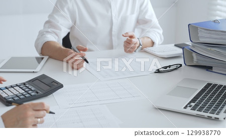 Two accountants collaborating in a well lit office, analyzing financial data and preparing reports with calculators and pens. Audit and taxes in business 129938770