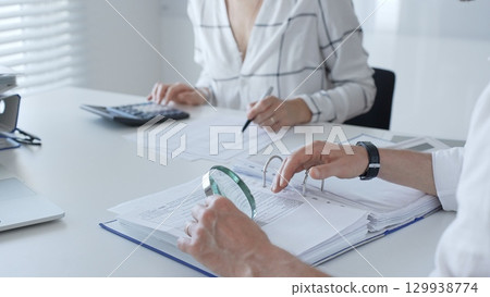 Team of professional accountants working together, using a magnifying glass and a calculators, to audit financial reports in their brightly lit office. Audit and taxes in business 129938774