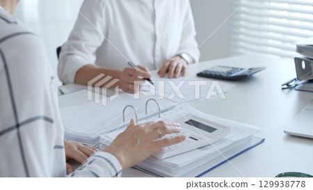 Two professional accountants colleagues are working together, using a magnifying glass and a calculators, to audit financial reports in office. Audit and taxes in business 129938778