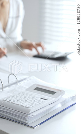 Close up of a calculator on financial documents, with an accountant taking notes, emphasizing accounting, finance, and tax preparation. Audit and taxes in business 129938780