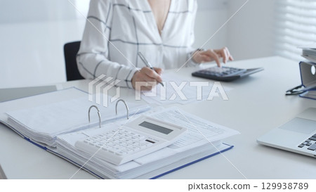 Calculator on financial documents, with an accountant taking notes, emphasizing accounting, finance, and tax preparation, close up. Audit and taxes in business 129938789