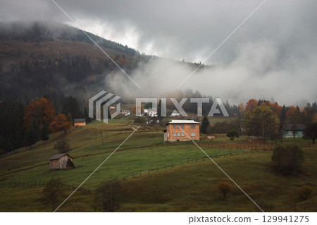 Mountain village in mountains on rainy day. Autumn landscape in Carpathian mountains. Tranquil rural landscape with autumn forest and local houses.  Foggy mountains and forest. Authentic Ukraine 129941275
