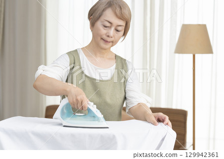 一位老年婦女在客廳熨燙襯衫 一位老年婦女在客廳熨燙襯衫 129942361