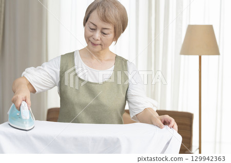 Senior woman ironing a shirt in the living room Senior woman ironing a shirt in the living room 129942363