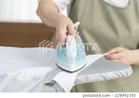Senior woman (no face) ironing a shirt in the living room 129942393