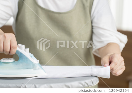 Senior woman (no face) ironing a shirt in the living room Senior woman (no face) ironing a shirt in the living room 129942394