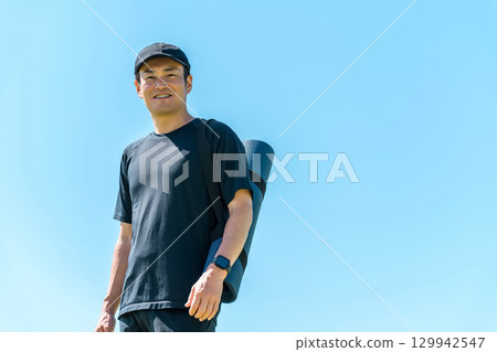 一個男人在藍天下拿著瑜珈墊（運動、運動、瑜珈、運動、伸展） 129942547