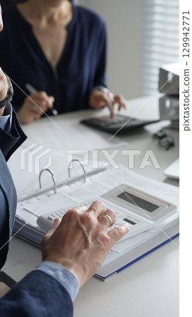 Close up of male accountant hands using calculator while collaborating with female colleague in office, calculating taxes and analyzing financial data. Audit and taxes concept Close up of male accountant hands using calculator while collaborating with female colleague in office, calculating taxes and analyzing financial data. Audit and taxes concept 129942771