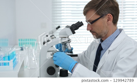 Medical scientist wearing gloves using microscope analyzing samples in modern laboratory doing scientific research. Medicine, healthcare and science concept Medical scientist wearing gloves using microscope analyzing samples in modern laboratory doing scientific research. Medicine, healthcare and science concept 129942789