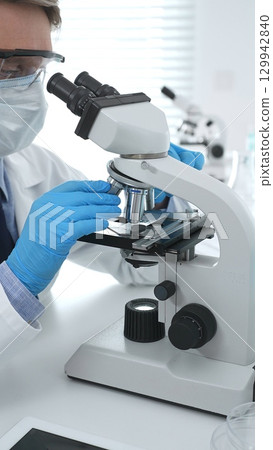 Man scientist wearing protective googles and blue gloves, is using microscope analyzing samples in modern laboratory doing scientific research. Medicine and science concept 129942840