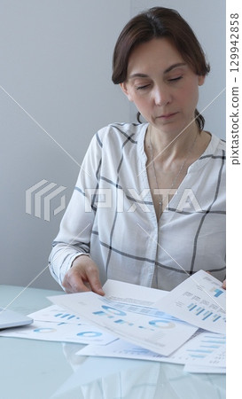Businesswoman reviewing financial data, analyzing charts and graphs while working on a project at her office desk, demonstrating focus and expertise in business management. Business people concept Businesswoman reviewing financial data, analyzing charts and graphs while working on a project at her office desk, demonstrating focus and expertise in business management. Business people concept 129942858