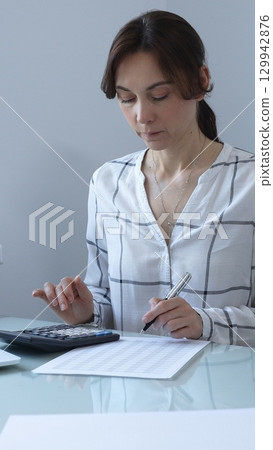 Female professional calculating finances, reviewing paperwork, tracking business expenses with precision and focus. Audit and taxes in business 129942876
