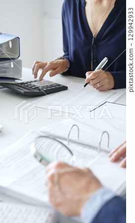Business colleagues are reviewing financial reports and using a calculator during a productive meeting in a brightly lit office setting. Audit and taxes in business 129942933