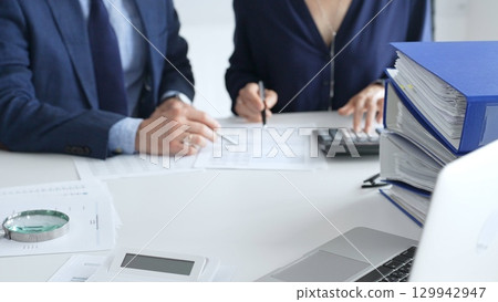 Close up of magnifying glass and calculator over financial documents opposite financial team, reviewing reports, collaborating on accounting details at modern office workspace. Audit and taxes 129942947