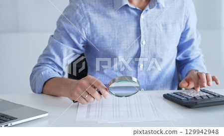 Professional businessman analyzing financial report, using magnifying glass and calculator for precise data verification and detailed performance assessment. Audit and taxes in business Professional businessman analyzing financial report, using magnifying glass and calculator for precise data verification and detailed performance assessment. Audit and taxes in business 129942948