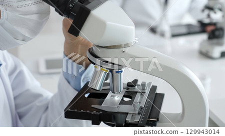 Gloved hands adjusting a microscope in a bright laboratory, emphasizing precision and focus in scientific research. Medicine, healthcare and science concept 129943014