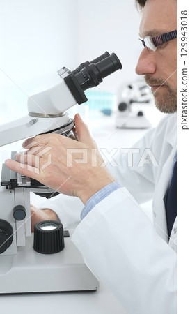 Medical scientist wearing glasses using microscope analyzing samples in modern laboratory doing scientific research. Medicine, health care and science concept Medical scientist wearing glasses using microscope analyzing samples in modern laboratory doing scientific research. Medicine, health care and science concept 129943018