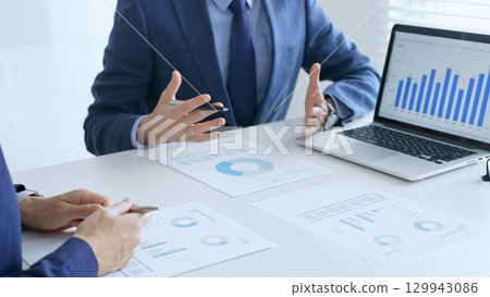 Business team analyzing financial data on a laptop and printed documents, pointing at charts and graphs during a meeting. Business people and finance concept 129943086
