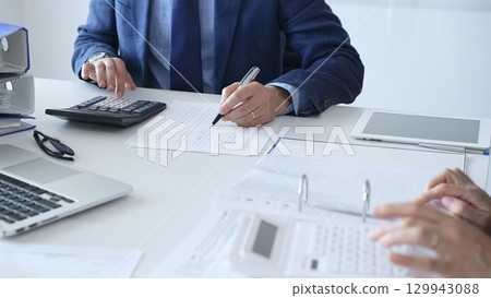Close up of female accountant hands using calculator while collaborating with male colleague in office, calculating taxes and analyzing financial data. Audit and taxes in business Close up of female accountant hands using calculator while collaborating with male colleague in office, calculating taxes and analyzing financial data. Audit and taxes in business 129943088