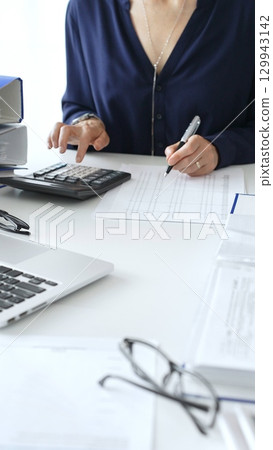 Female financial analysts examining documents, using magnifying glass and calculator while studying corporate data at workplace. Audit and taxes Female financial analysts examining documents, using magnifying glass and calculator while studying corporate data at workplace. Audit and taxes 129943142