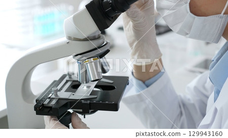 Gloved hands adjusting a microscope in a bright laboratory, emphasizing precision and focus in scientific research. Medicine, healthcare and science concept Gloved hands adjusting a microscope in a bright laboratory, emphasizing precision and focus in scientific research. Medicine, healthcare and science concept 129943160