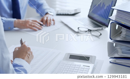 Two professional accountants analyzing financial documents and using a calculator with a laptop in a bright office. Audit and taxes in business Two professional accountants analyzing financial documents and using a calculator with a laptop in a bright office. Audit and taxes in business 129943181