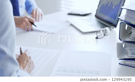 Corporate professionals reviewing financial documents, working collaboratively at white desk with blue folder stack, highlighting teamwork and business productivity. Audit and taxes in business Corporate professionals reviewing financial documents, working collaboratively at white desk with blue folder stack, highlighting teamwork and business productivity. Audit and taxes in business 129943295
