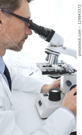 Medical scientist wearing glasses using microscope analyzing samples in modern laboratory doing scientific research. Medicine, health care and science concept Medical scientist wearing glasses using microscope analyzing samples in modern laboratory doing scientific research. Medicine, health care and science concept 129943372