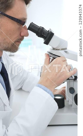 Medical scientist wearing glasses using microscope analyzing samples in modern laboratory doing scientific research. Medicine, health care and science concept 129943374