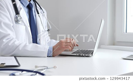 Medical professional typing on laptop, updating electronic patient records with focused concentration, representing digital transformation in healthcare workplace Medical professional typing on laptop, updating electronic patient records with focused concentration, representing digital transformation in healthcare workplace 129943417